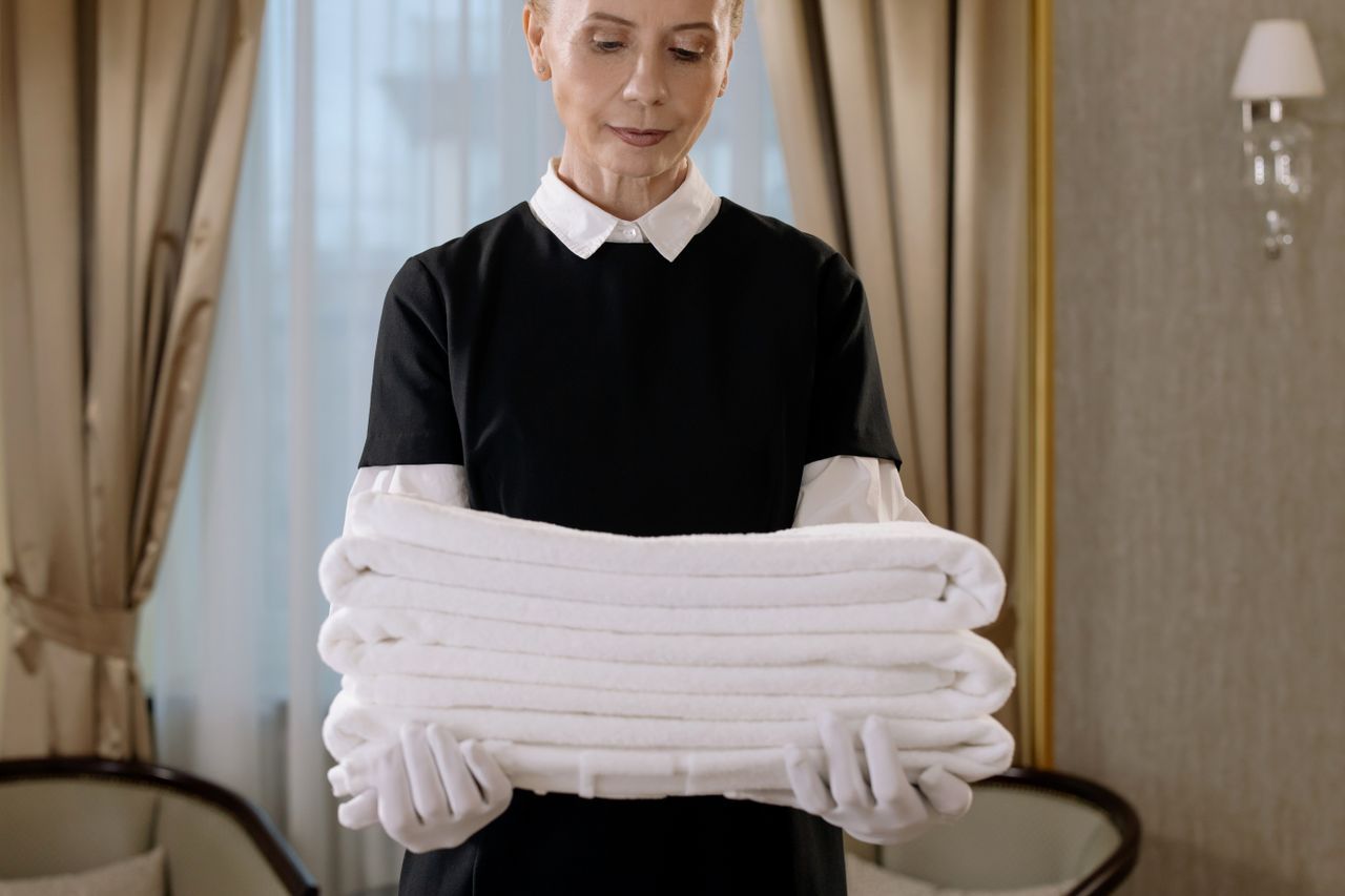 who-we-are Professional housekeeper holding a stack of fresh towels in a luxurious hotel room, showcasing elegance and service.