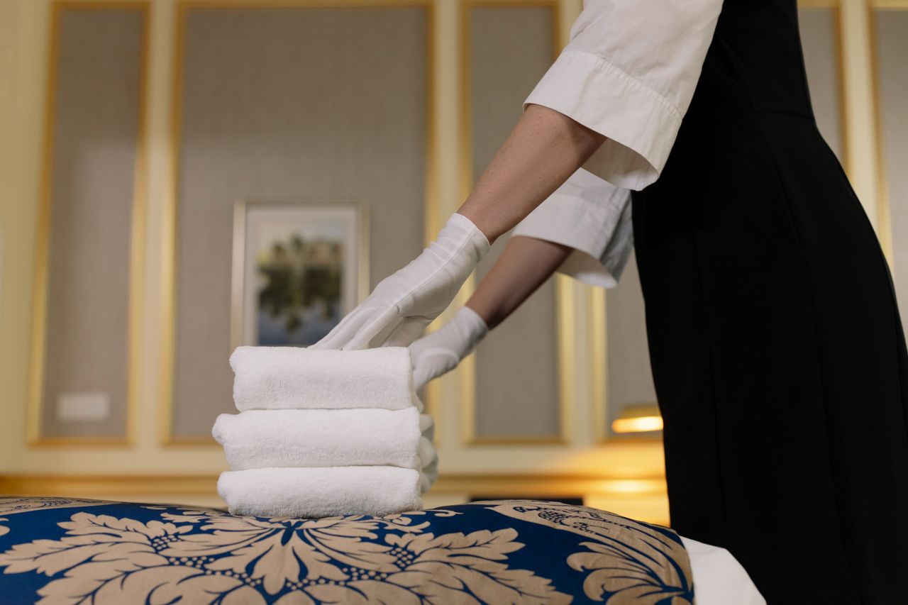 our-story A hotel housekeeper neatly stacks fresh towels in a luxurious room setting.