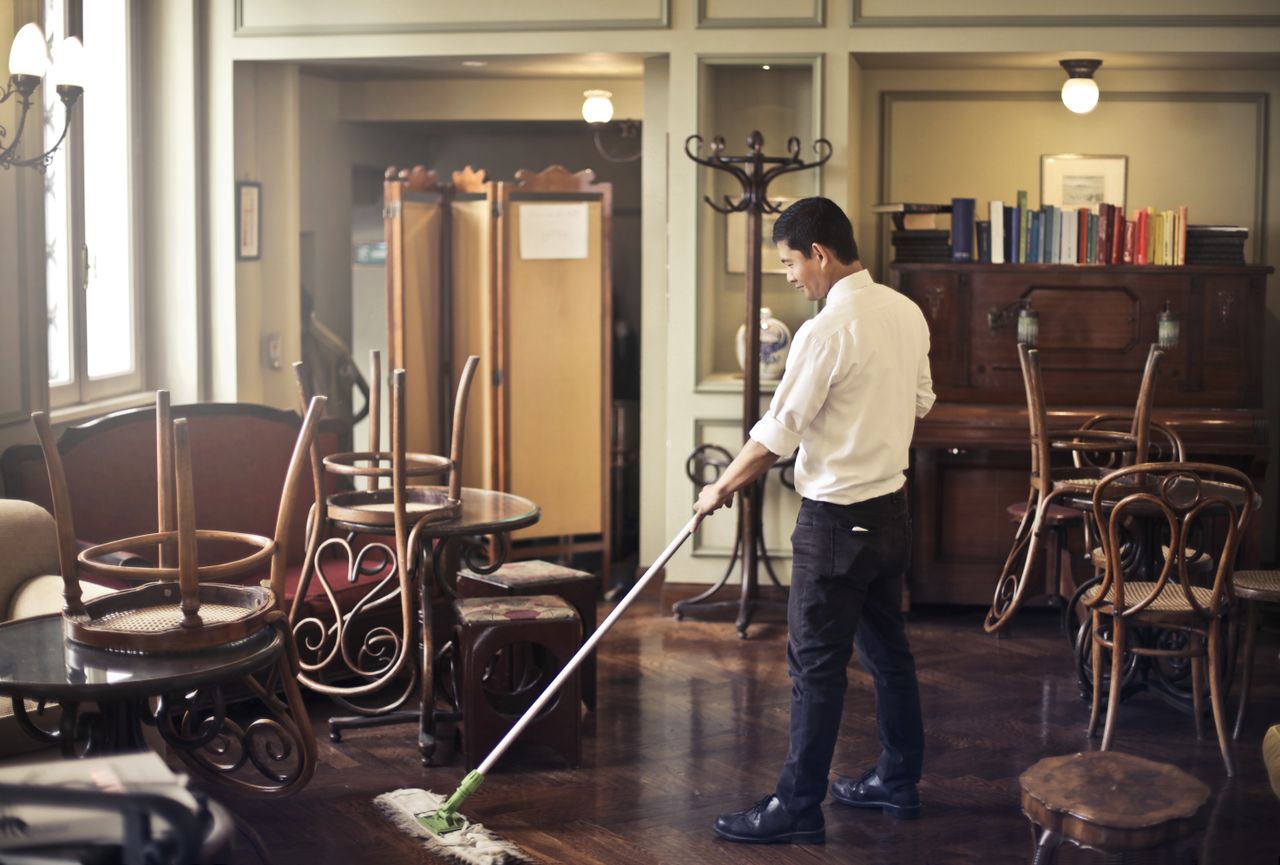heros-img Side view of young ethnic male in uniform cleaning floor with mop while working in retro styled restaurant